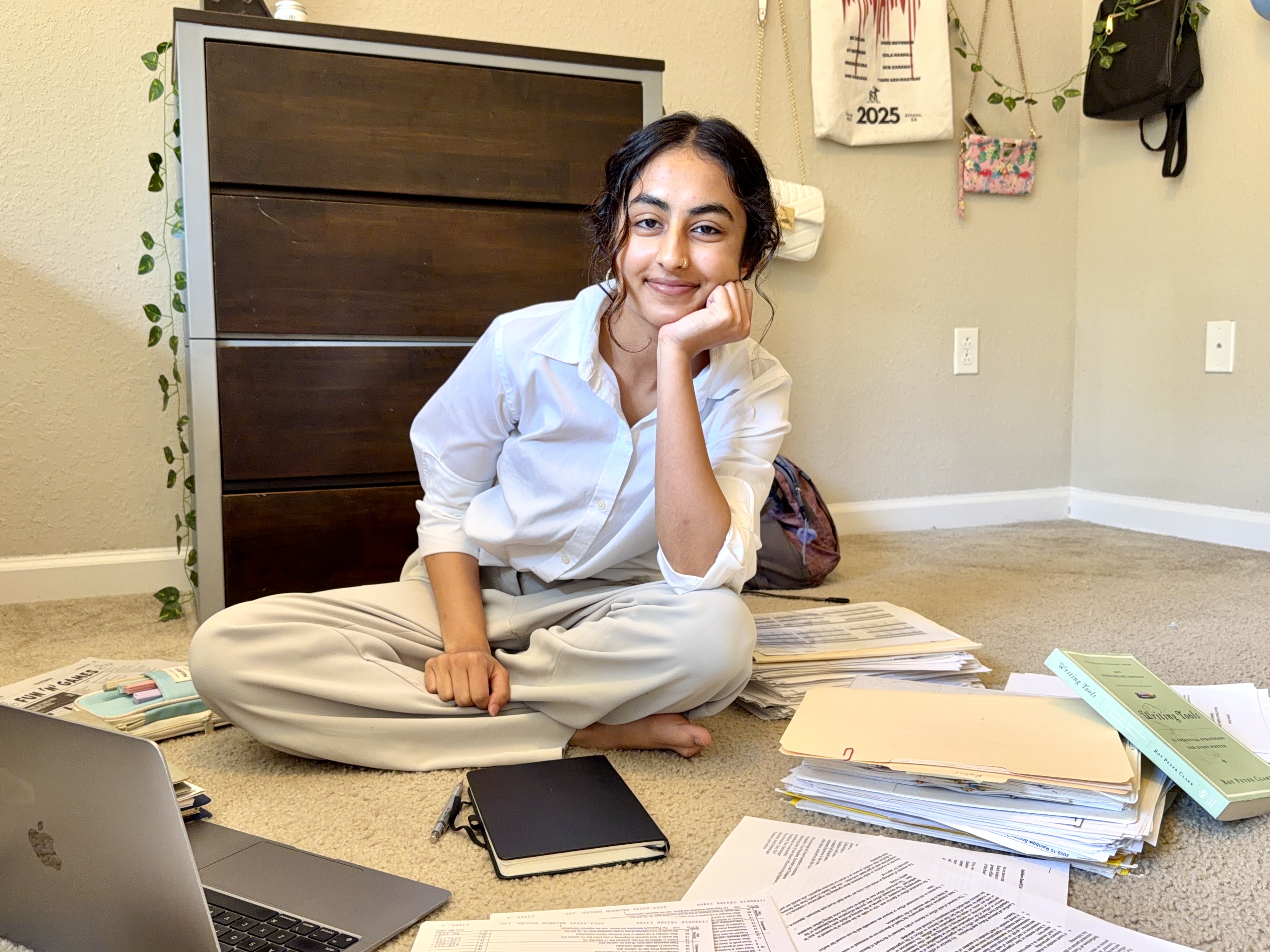 Keya sitting in the middle of books and files, smiling at the camera, chin resting on hand